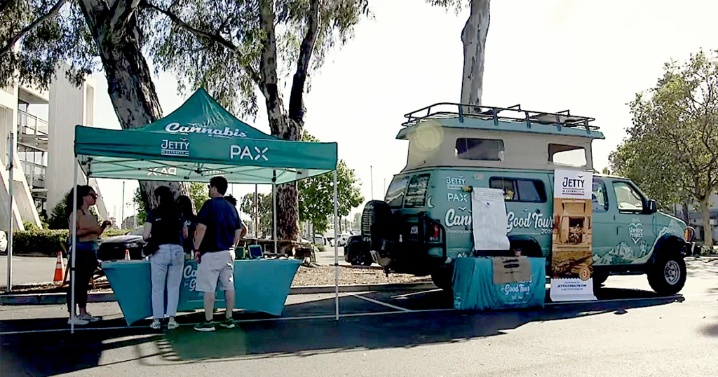 A Jetty Extracts and PAX “Cannabis for Good Tour” pop-up event featuring a teal canopy tent, outreach table, and the Shelter Project van parked beside it, promoting compassionate cannabis advocacy and patient access under California’s SB 34 Compassionate Care Act.