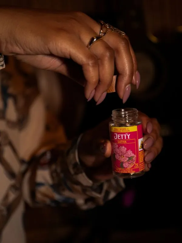 Close up of a hand taking the wood lid off off a pink Jetty pre-roll jar.