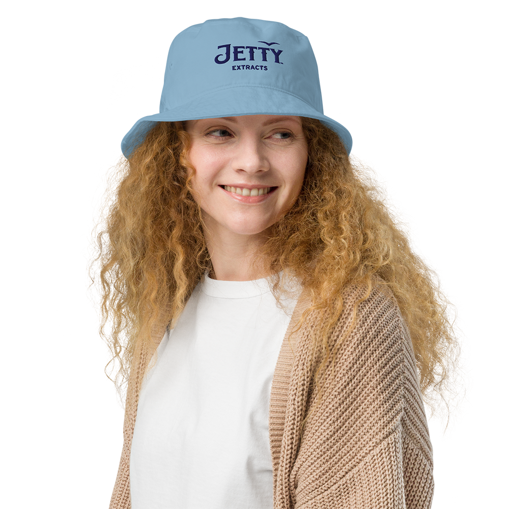 Woman wearing a light blue Jetty Extracts bucket hat with navy embroidered logo outdoors