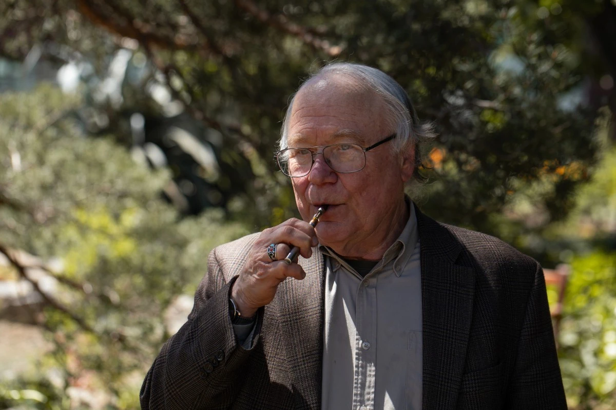 a senior man in a tweed jacket and glasses uses a JETTY Extracts vape pen outdoors.