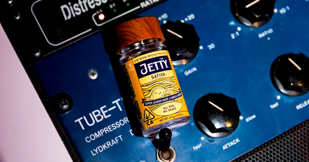 A Jetty Sativa High-THC infused pre-roll jar labeled “Super Lemon Haze x Garlic Grove” rests on a vintage TUBE-TECH audio compressor, symbolizing the connection between handcrafted cannabis and music studio production.