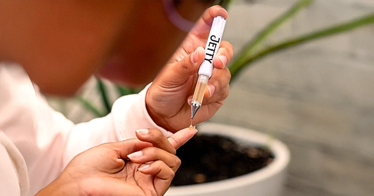 Person dispensing a small drop of cannabis oil from a Jetty Extracts Dablicator onto their fingertip, demonstrating precise oral dosing in a casual indoor setting