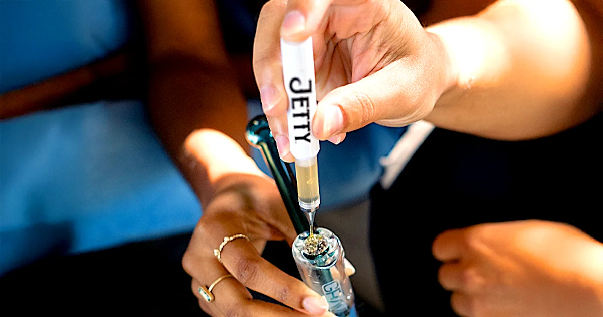 Person using a Jetty Extracts Dablicator to add cannabis oil onto a packed bowl of flower in a glass Sherlock pipe, demonstrating how to top flower with marijuana oil concentrate