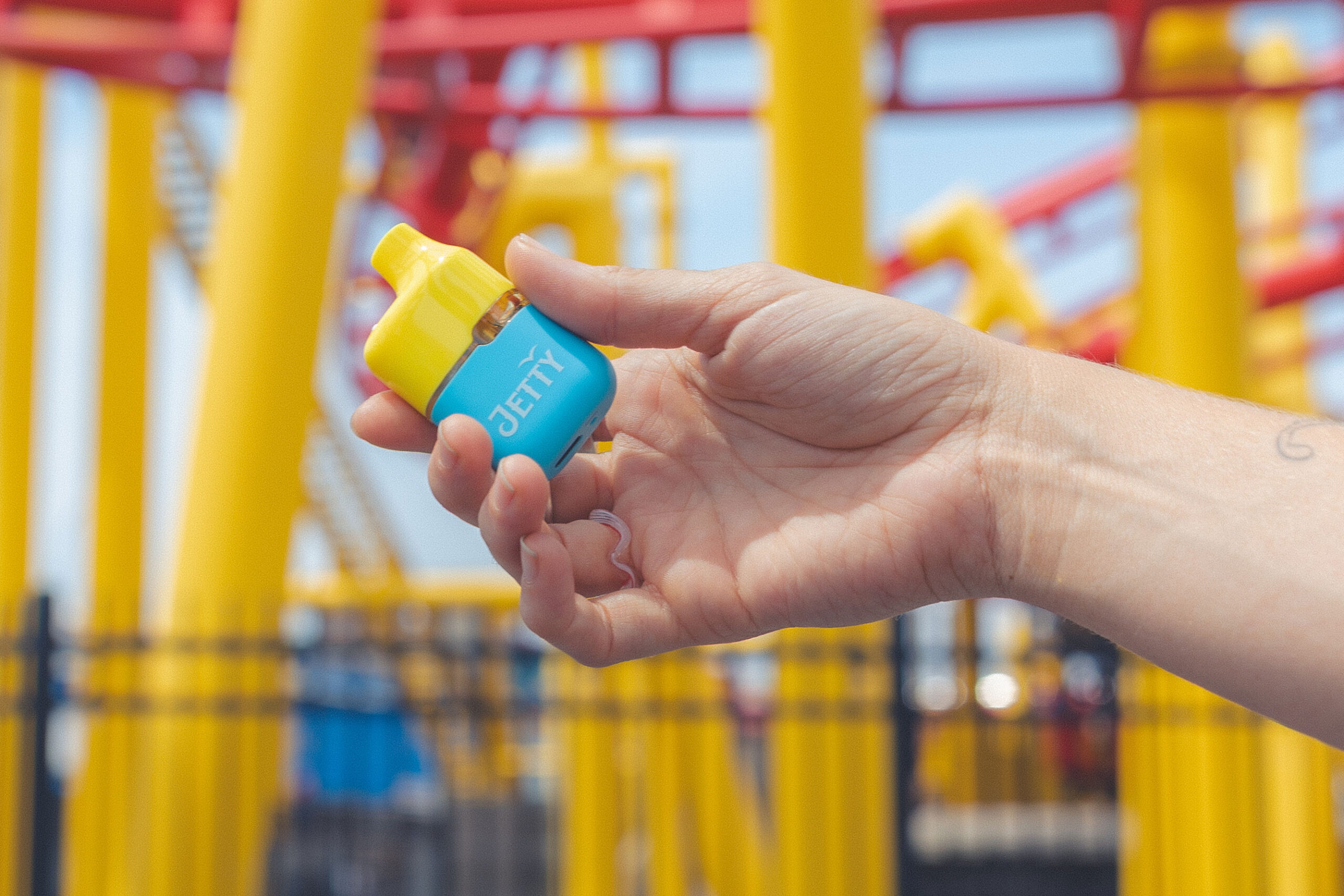 Hand holding a blue and yellow Jetty High THC Mega Tank 2g vape.